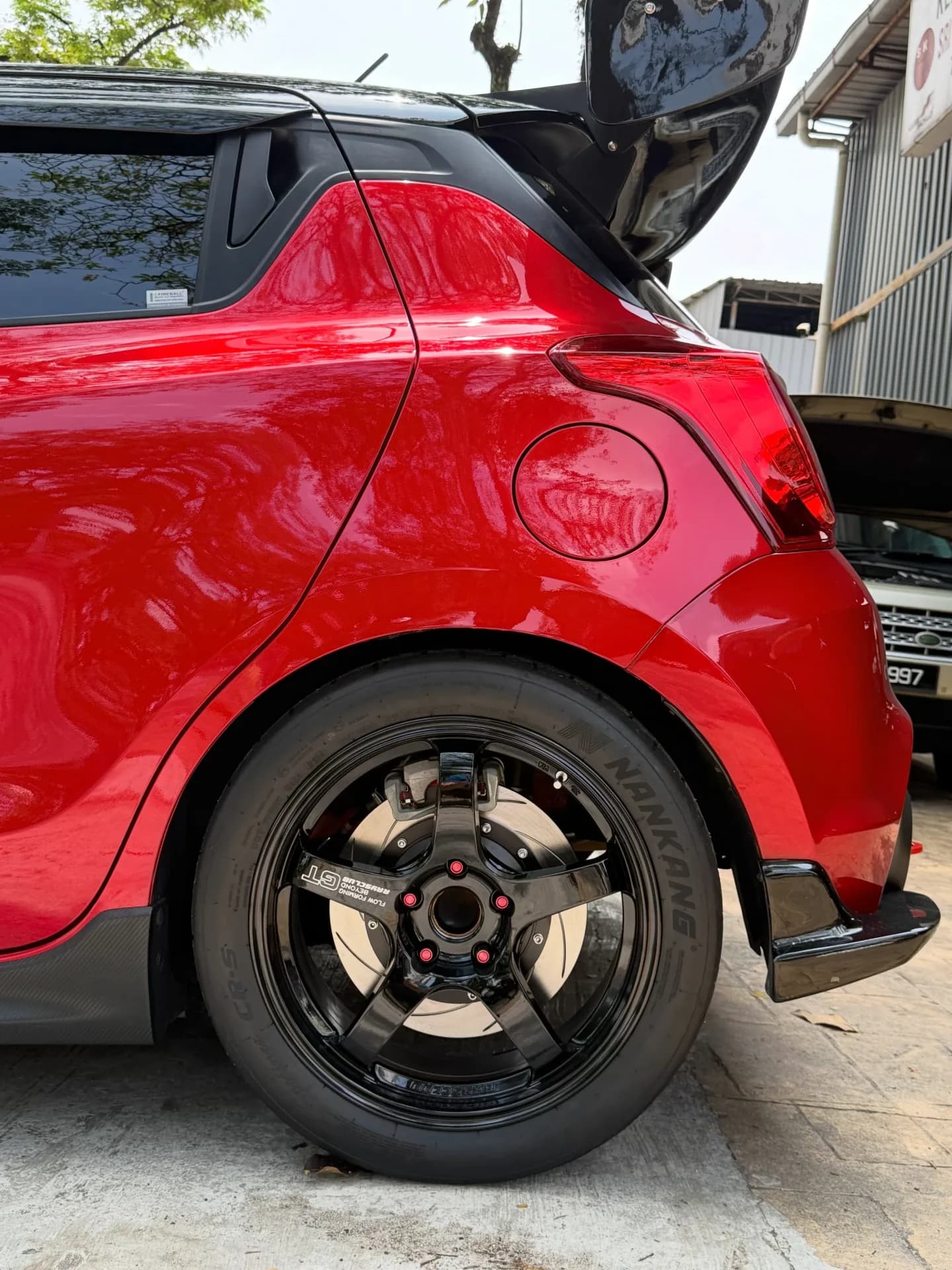 Rear quarter of the red Suzuki Swift Sport showing its dark alloy wheel at the workshop